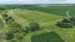 Aerial view of a 30-acre Washington County parcel for sale, featuring a central grassland plateau bordered by lush row-crop fields, scattered trees, and rolling farmland.