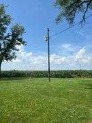 Ground-level photo of a wooden utility pole with transformer and overhead service line set in a mown farmyard, with cornfields and blue sky—part of a 42-acre Washington County farm for sale.