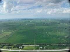 Aerial view of a 72-acre Washington County, Iowa row-crop field for sale—uniform green soybeans on gently rolling ground bordered by grass waterways and a nearby paved highway.