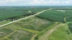 Elevated drone photo of a 27-acre Washington County, Iowa parcel for sale, showing concentric contour-planted fields, grass waterways, and long frontage on a paved highway.