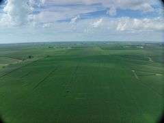 Wide drone view of expansive, uniform soybean fields in Washington County, Iowa—72 acres of contiguous cropland stretching toward a distant highway and rolling farmland.
