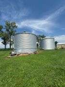Drone view of two silver, corrugated-steel grain bins on a neatly mown farmyard, framed by tall cornfields—part of a 42-acre Washington County, Iowa farm for sale.
