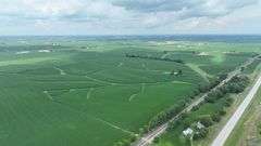 Aerial drone view of 70 contiguous acres of Washington County cropland for sale—lush soybean fields patterned with branching grass waterways and bordered by a tree-lined rail spur.
