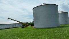 Drone view of two silver, corrugated-steel grain bins on a neatly mown farmyard, framed by tall cornfields—part of a 42-acre Washington County, Iowa farm for sale.
