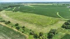 Aerial view of a 30-acre Washington County parcel for sale, featuring a central grassland plateau bordered by lush row-crop fields, scattered trees, and rolling farmland.