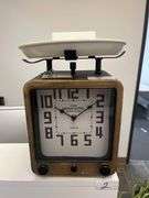 vintage scale clock with a wooden frame, large black numerals, and a white weighing platform on top.